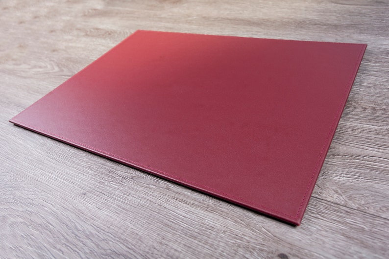 May include: A burgundy leather desk mat. The mat is flat and rectangular with stitched edges.