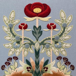 May include: Detailed embroidery of a floral pattern. A large red rose is at the top, with symmetrical arrangements of leaves, buds, and smaller flowers in green, blue, and brown. The design is set against a light blue fabric background.