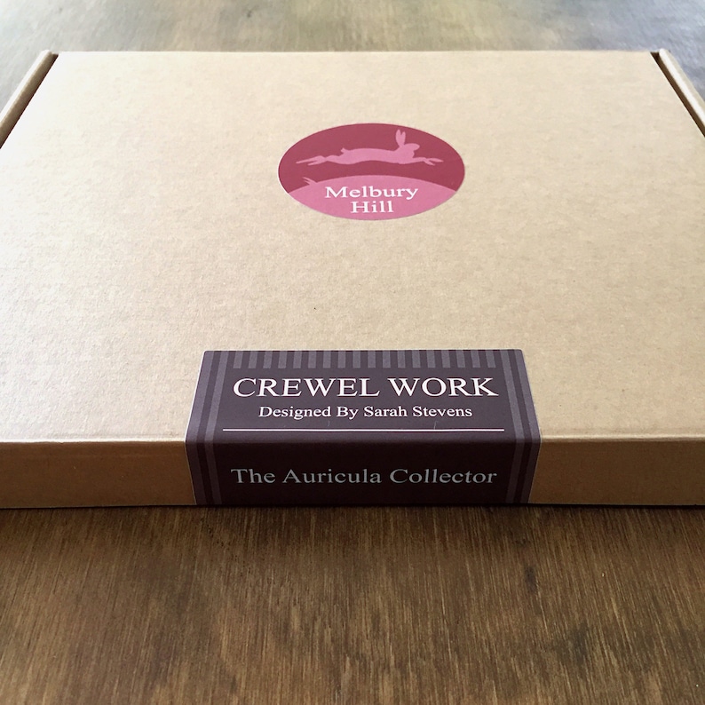 May include: A brown cardboard box with a red and white logo that says "Melbury Hill" and a brown label that says "CREWEL WORK Designed By Sarah Stevens The Auricula Collector"