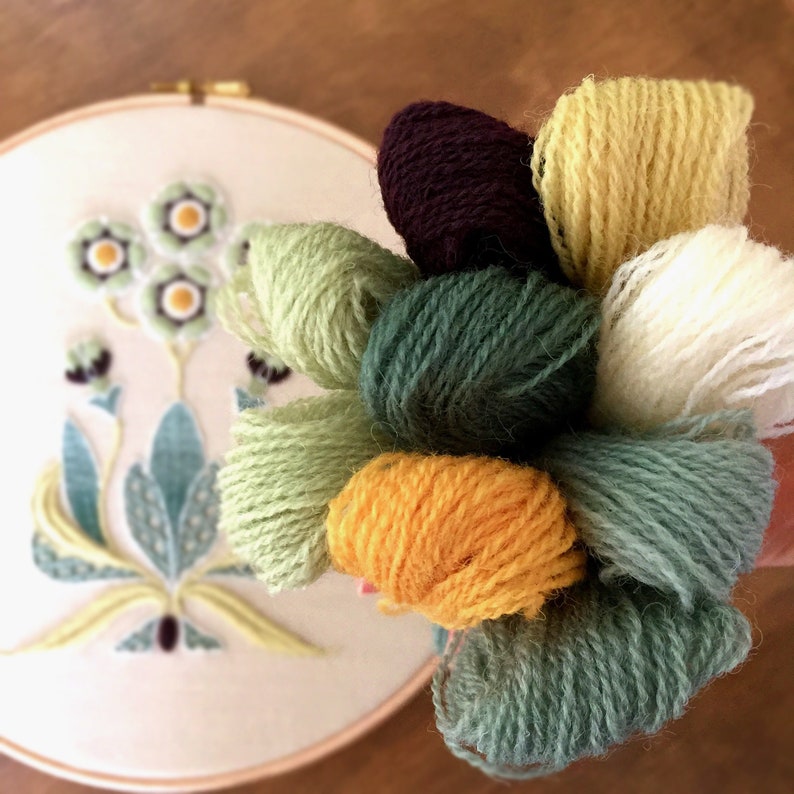 May include: A collection of embroidery floss in various shades of green, yellow, white, and brown. The floss is wound into balls and arranged in a bouquet.