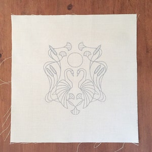May include: A white fabric with a gray line drawing of two swans with their necks intertwined, surrounded by stylized leaves and reeds. The design is centered on the fabric.