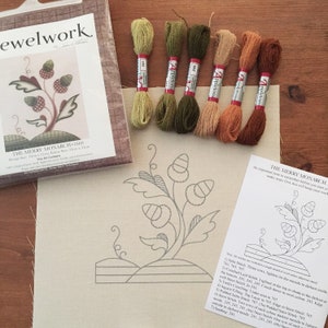 May include: A cross-stitch embroidery kit titled "The Merry Monarch 1660" with a printed design of a stylized floral motif with acorns. The kit includes six skeins of embroidery floss in shades of green, brown, and orange.