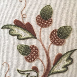 May include: Close-up of an embroidered design featuring a brown stem with green leaves and brown and green acorns.