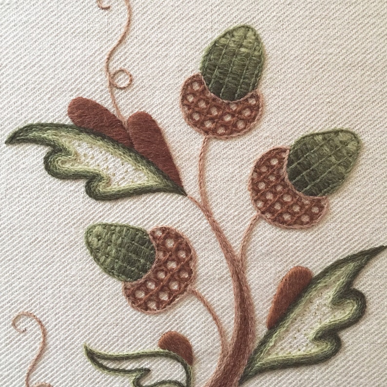 May include: Close-up of an embroidered design featuring a brown stem with green leaves and brown and green acorns.