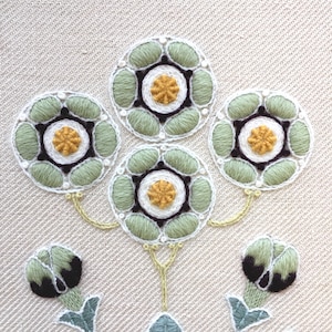 May include: Close-up of a green and white embroidered design with a floral motif. The design features five flowers with yellow centers and black outlines. The flowers are connected by green stems.