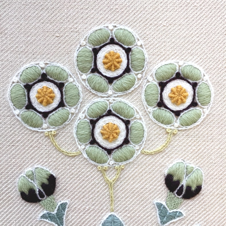 May include: Close-up of a green and white embroidered design with a floral motif. The design features five flowers with yellow centers and black outlines. The flowers are connected by green stems.