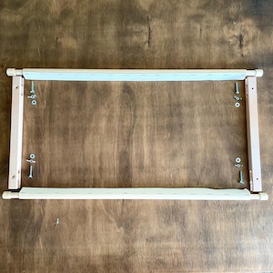 May include: A wooden embroidery hoop with white fabric stretched across the frame. The hoop is assembled on a wooden surface.