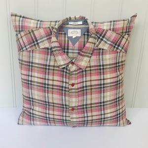 May include: A pillow made from a plaid shirt with red buttons. The shirt is a mix of pink, brown, and white plaid.