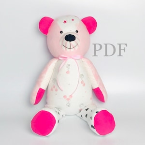 May include: A pink and white patchwork teddy bear with black eyes and a black nose. The bear is wearing a pink ribbon around its neck and has a white fabric with a pattern of pink balloons on its body. The bear is sitting on a white background. PDF.