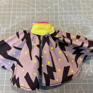 Könnte beinhalten: Ein grauer und schwarzer Rock mit gelbem Tupfenmuster und schwarzem Blitzmuster. Der Rock hat einen grünen Bund und eine lila Schleife.