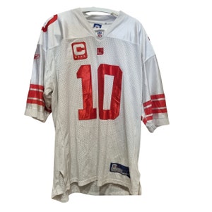 May include: White football jersey with red and blue accents. The jersey has the number "10" on the front and the New York Giants logo on the chest. The jersey is made by Reebok and has the NFL shield logo on the front.