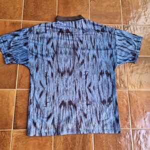 Puede incluir: Una camisa de manga corta azul y negra con estampado y cuello.