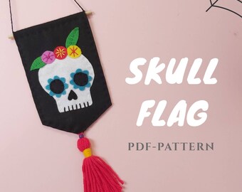 May include: A black felt flag with a white sugar skull with blue eyes and a flower crown. The flag has a red tassel and the text "SKULL FLAG PDF-PATTERN" is printed below.