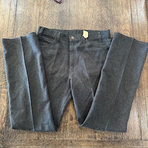 May include: Dark gray trousers with a button closure and a small tag attached. The pants have a classic five-pocket design and a straight leg. The fabric appears to be a medium-weight material, suitable for various occasions.