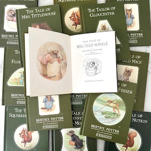 Op de afbeelding: Een verzameling vintage Beatrix Potter-boeken met groene covers en illustraties. Eén boek is open en toont een kleurenillustratie en de titel "The Tale of Mrs. Tiggy-Winkle". Andere titels zijn onder meer "The Tale of Squirrel Nutkin".