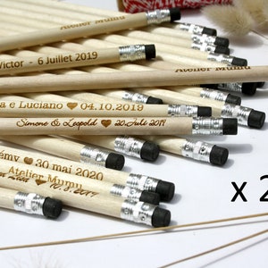 Puede incluir: Un paquete de 25 lápices de madera con mensajes personalizados para bodas y otras ocasiones especiales. Los lápices son de madera natural con gomas negras y detalles metálicos plateados. El texto en los lápices incluye nombres, fechas y la frase "Atelier Muru".