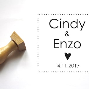 Puede incluir: Un sello de madera con mango y base rectangular. El sello dice "Cindy & Enzo" con un símbolo de corazón y la fecha "14.11.2017".