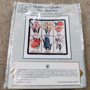 May include: A needlepoint kit featuring a floral design with various flowers, including crocus, tulips, and iris. The kit is labeled "Heirloom Quality Needlepoint" and includes the text "Spring Botanical." The package is sealed in clear plastic.