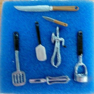May include: Miniature kitchen utensils set, including a knife, spatula, whisk, and more. The set features silver and black handles with a brown knife handle, all arranged on a blue surface. Perfect for dollhouses or craft projects.