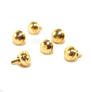 May include: Six small, gold-colored, round-shaped decorative furniture knobs with a screw post. The knobs have a smooth, shiny finish and are scattered on a white background. The knobs are likely used for drawers or cabinets.