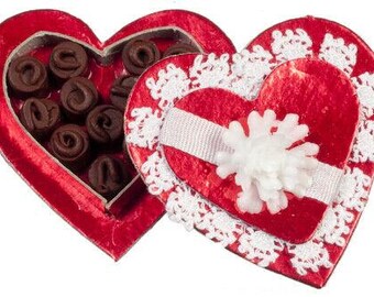 May include: A red heart-shaped box of chocolates, with a matching lid decorated with white lace and a white ribbon. The box is filled with dark chocolate candies. A festive gift for Valentine's Day or a special occasion.