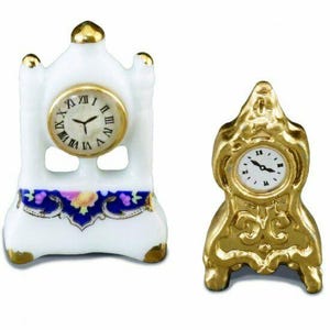 May include: Two miniature decorative clocks. One is white with gold accents and a floral design, the other is gold. Both have Roman numeral clock faces and are set against a white background.