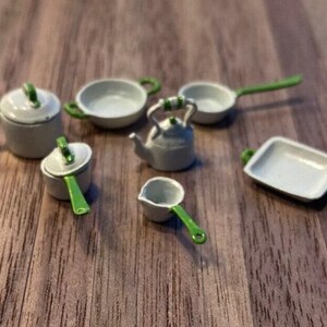 May include: Miniature kitchen cookware set with white and gray pots, pans, and a kettle. The handles and accents are bright green. The set includes a saucepan, a frying pan, a small pot with a lid, a kettle, a small dish, and a rectangular baking dish.
