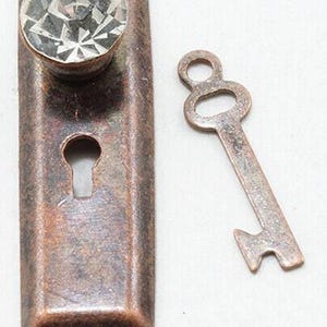 May include: A vintage-style keyhole plate with a large, faceted crystal knob and a small, decorative key. The keyhole plate and key have a rustic, bronze finish. The key is a simple, skeleton key design.