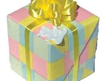 May include: A pastel-colored gift box wrapped in pink, yellow, and blue stripes, topped with a large yellow bow. A white teddy bear-shaped embellishment is affixed to the box, which is tied with a yellow ribbon.