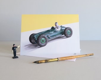 Puede incluir: Un coche de carreras de juguete verde con un conductor con un traje de carreras blanco. El coche está sobre un fondo amarillo y blanco. La imagen está en una tarjeta de felicitación.