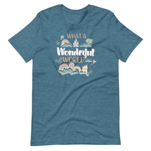 May include: A teal blue t-shirt with the text "What a Wonderful World" in a whimsical font. The text is surrounded by colorful illustrations of a castle, clouds, rainbows, and stars.