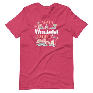 May include: A pink heather t-shirt with the text "What a Wonderful World" in a whimsical font. The text is surrounded by colorful illustrations of clouds, rainbows, and a castle.