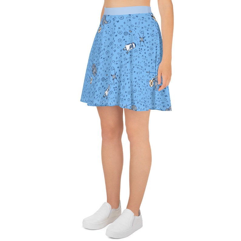 Puede incluir: Una falda skater azul claro con un patr&oacute;n caprichoso de gatos, estrellas y otros garabatos.