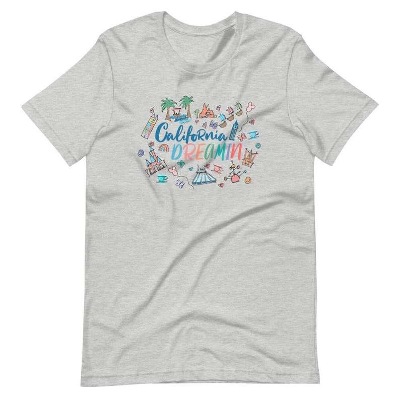 May include: A heather grey t-shirt with a colorful doodle design featuring California Dreamin' text and various California-themed icons, including palm trees, a Ferris wheel, a castle, and a surfboard.