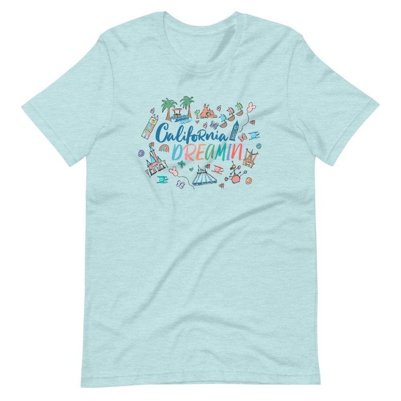 May include: Light blue t-shirt with a colorful graphic design featuring the text "California Dreamin'" and various cartoon images of attractions and landmarks.