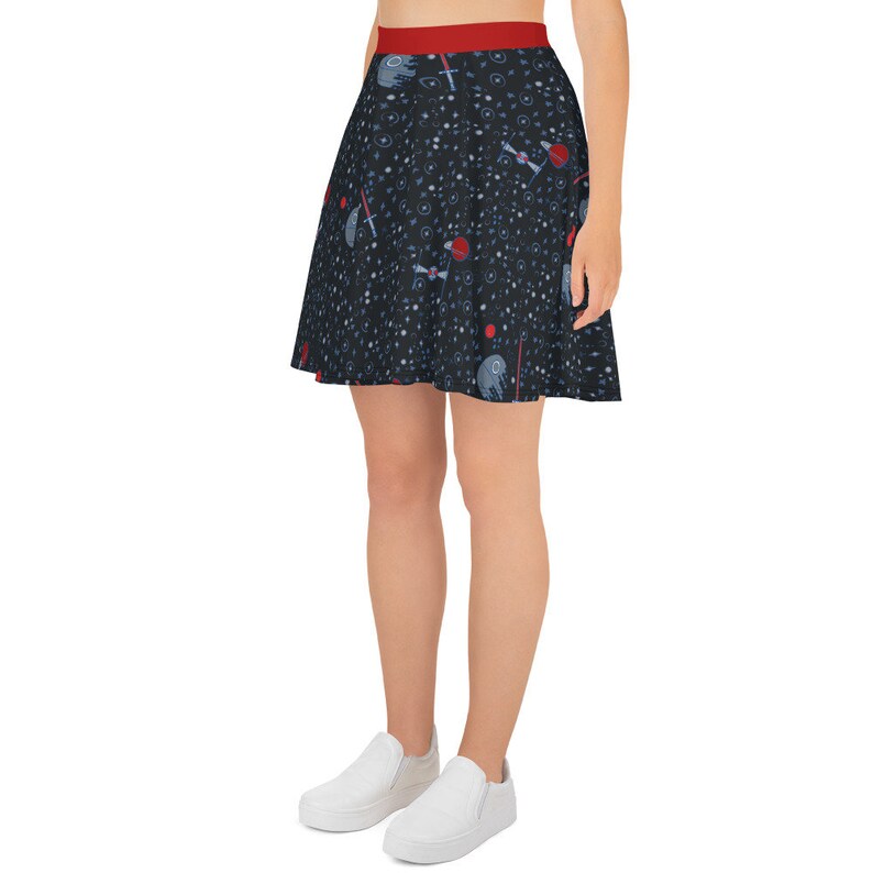 May include: A black skater skirt with a space-themed print featuring stars, planets, and spaceships. The skirt has a red waistband.