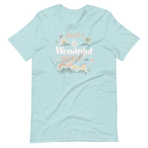 May include: A light blue t-shirt with a whimsical design featuring a castle, rainbows, and the text "What a Wonderful World".