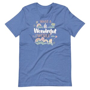 May include: A blue t-shirt with the text "What a Wonderful World" in pink and orange lettering. The shirt features a whimsical design with a castle, rainbows, and clouds.