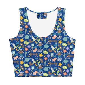 May include: A blue sleeveless crop top featuring an all-over pattern of cartoon characters, including green three-eyed aliens, potato-shaped figures, brown dachshunds, rockets, cacti, stars, planets, horseshoes, and alphabet blocks in various colors.