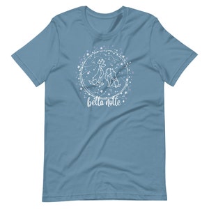 Puede incluir: Una camiseta azul claro con un dise&ntilde;o blanco de dos perros y estrellas en un c&iacute;rculo. El texto "bella notte" est&aacute; escrito debajo del c&iacute;rculo.