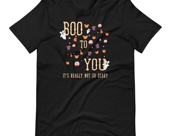 Może przedstawiać: Czarny t-shirt z napisem "BOO TO YOU" i "IT'S REALLY NOT SO SCARY" w halloweenowym designie. Projekt zawiera duchy, babeczki i cukierki. Zabawna koszulka na straszny sezon.