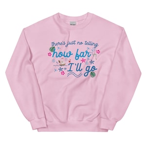 May include: A light pink sweatshirt with the text "there's just no telling how far I'll go" in blue script. The design includes tropical elements like flowers, starfish, and a boat. The sweatshirt is made of a soft material.
