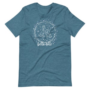 Puede incluir: Una camiseta azul turquesa con un dise&ntilde;o blanco de tres perros en un c&iacute;rculo de estrellas. El texto "bella notte" est&aacute; debajo del c&iacute;rculo.