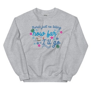 May include: A light gray sweatshirt with the text "there's just no telling how far I'll go" in blue and turquoise script. The design includes tropical flowers, a boat, and starfish.