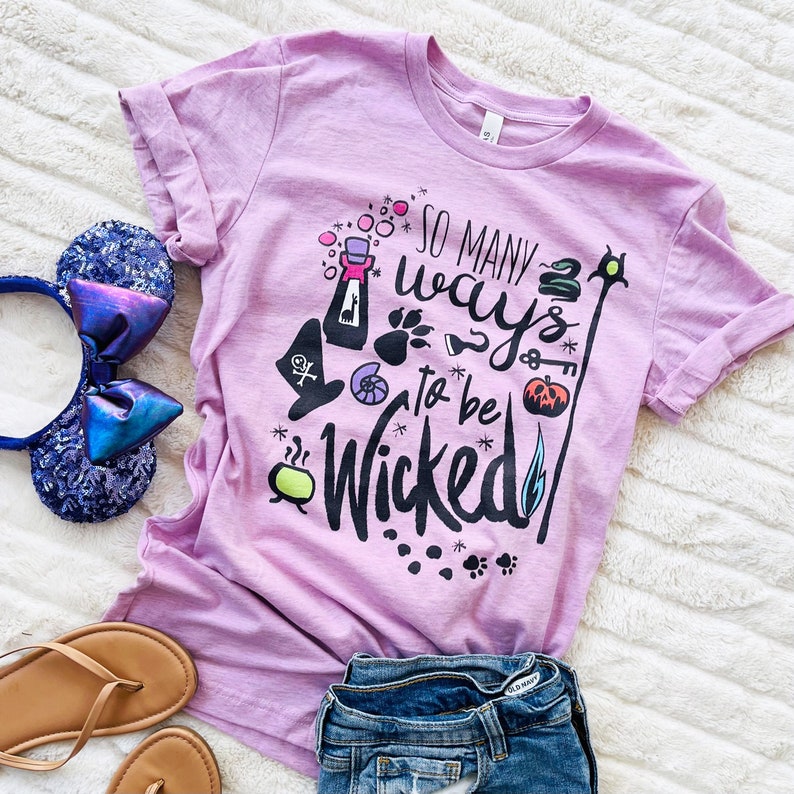 May include: A purple t-shirt with the text "So many ways to be wicked" in black with colorful illustrations of Halloween-themed items.