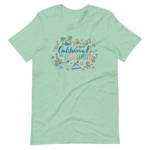 May include: A light green t-shirt with a colorful illustration of a California theme park. The text "California Dreamin'" is written in a rainbow font.