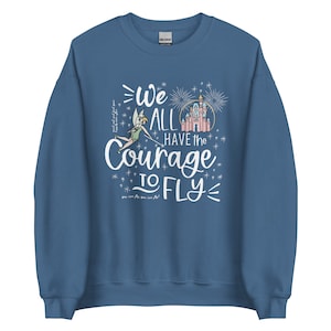 May include: A blue sweatshirt with a white graphic of Tinkerbell flying with the text "We All Have the Courage to Fly" and a pink castle with fireworks in the background.