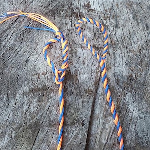May include: Two pieces of blue and orange braided rope, one tied in a knot and the other in a loop, against a wooden background.