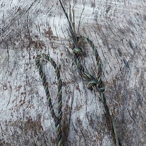 May include: Two pieces of camouflage rope, one tied in a knot, on a weathered wooden surface.
