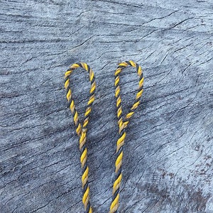 May include: Two pieces of yellow and black braided rope with loops at the ends, lying on a weathered gray wooden surface.